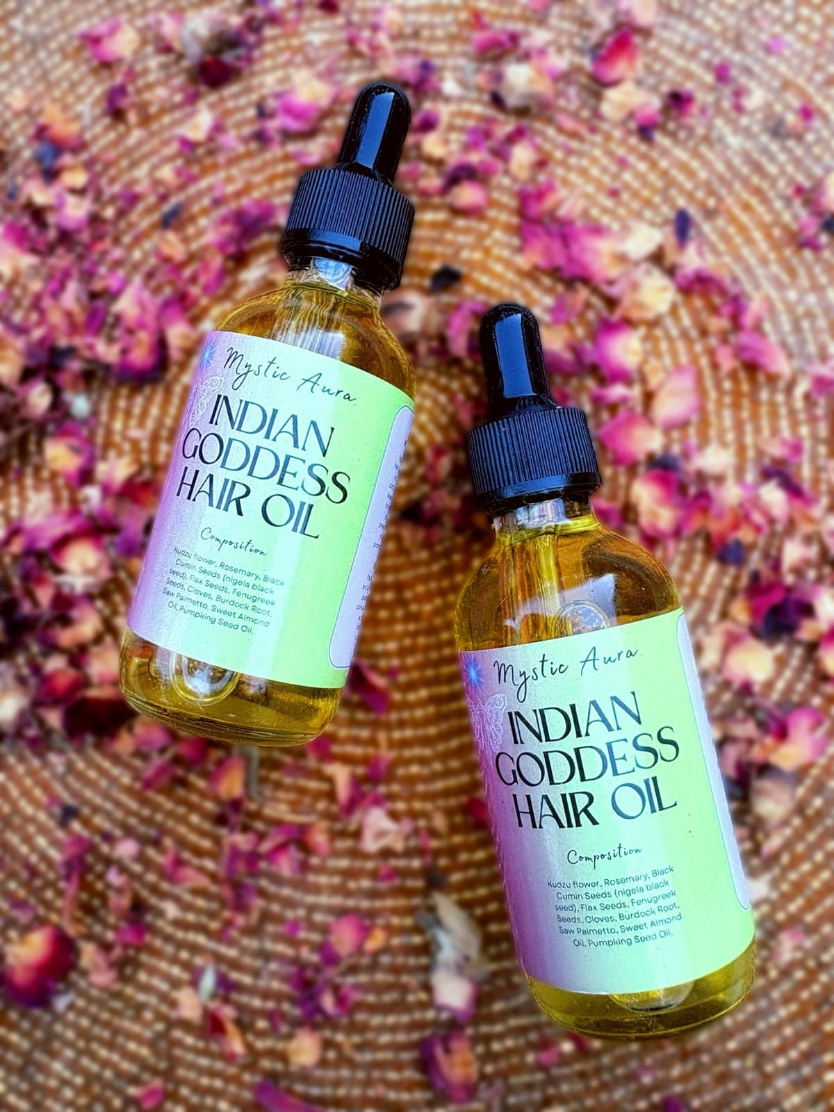 Top-down view of two Indian Goddess Hair Oil bottles among scattered petals